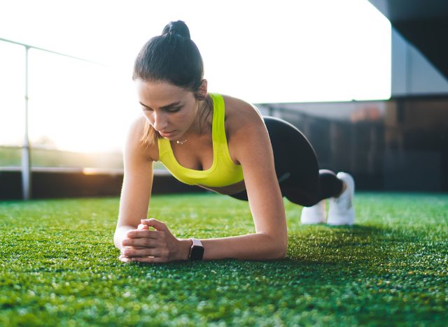 Concentrated female athlete in activewear doing plank exercises training muscle strength outdoors, energetic sporty woman having workouts do effort balancing losing weight and gain physical power