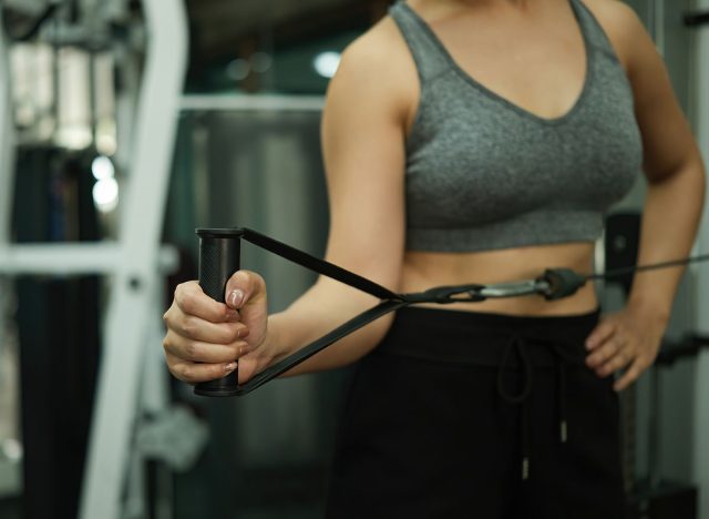 Close-up of a woman performing shoulder external rotation with a cable machine for strengthening muscles and improving shoulder stability during fitness training.