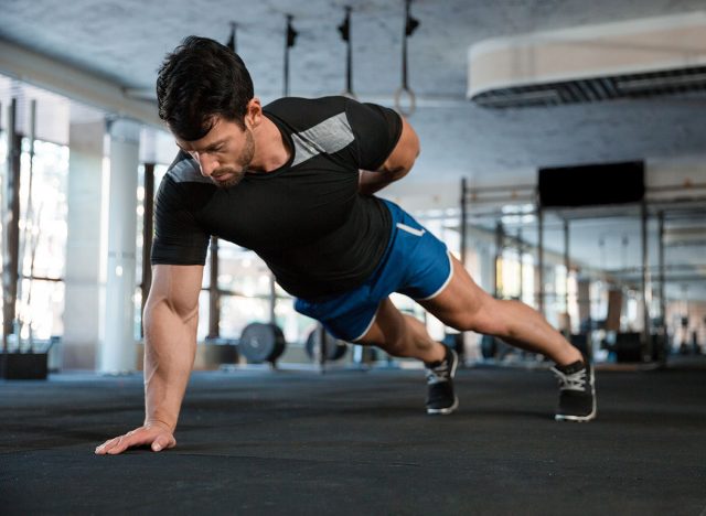 Athlete wearing blue shorts and black t-shirt doing one hand push-ups
