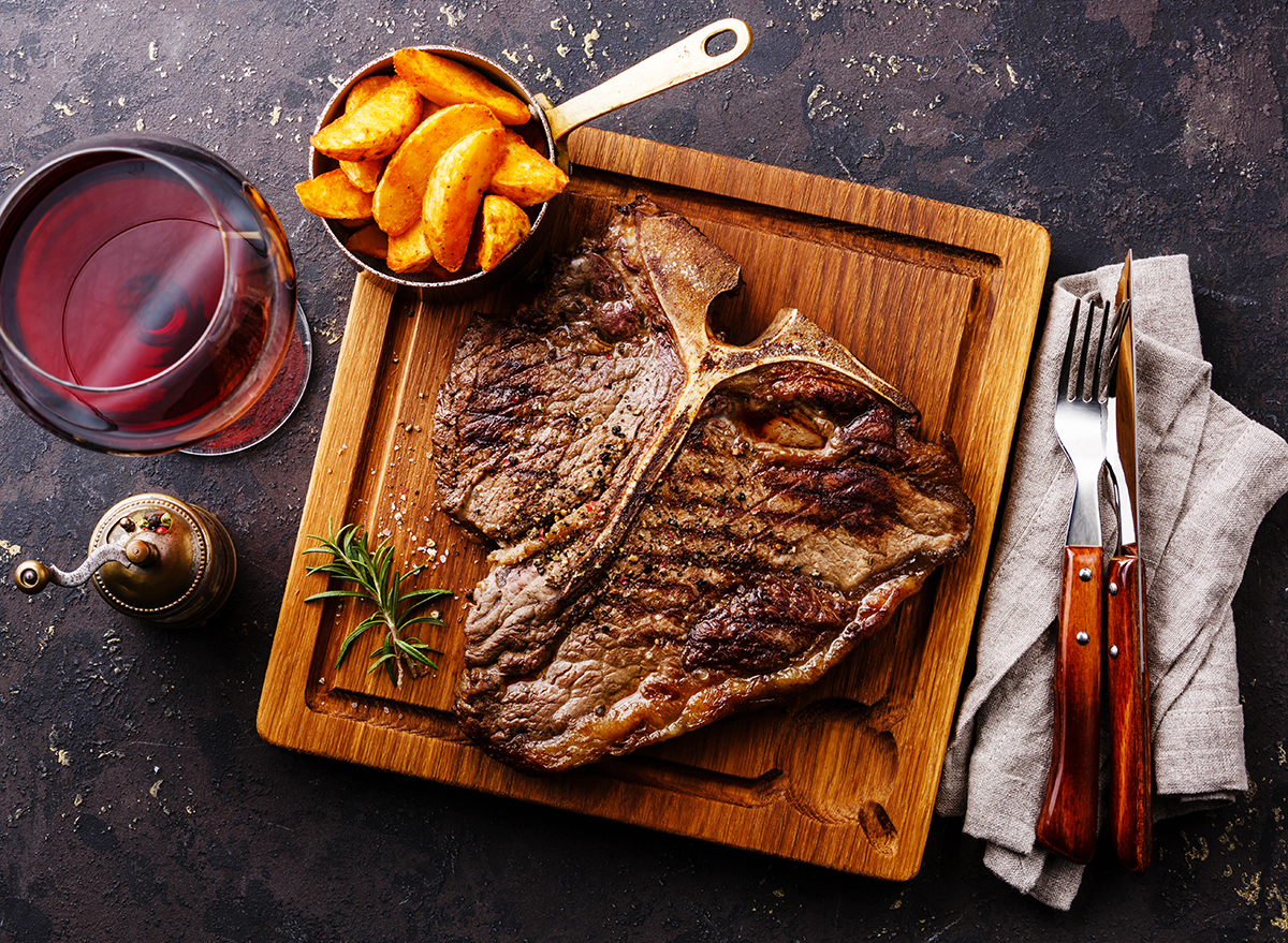 Medium rare Grilled T-Bone Steak with potato wedges and wine on serving board block on dark background