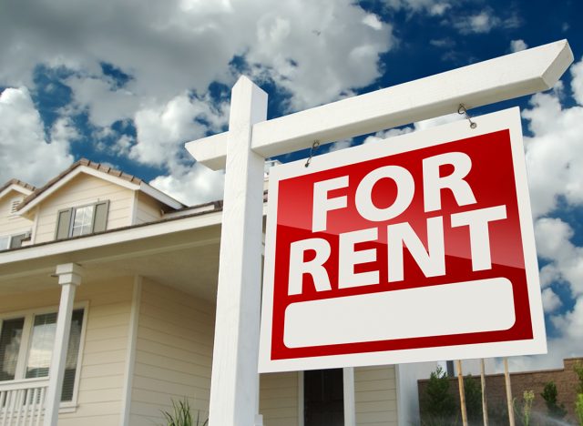 Left Facing Red For Rent Real Estate Sign in Front of Beautiful House.