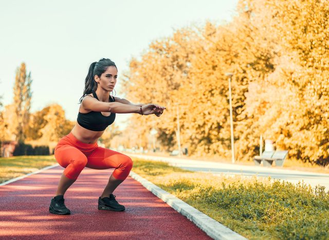 Young motivated female doing squats in the park outdoor.