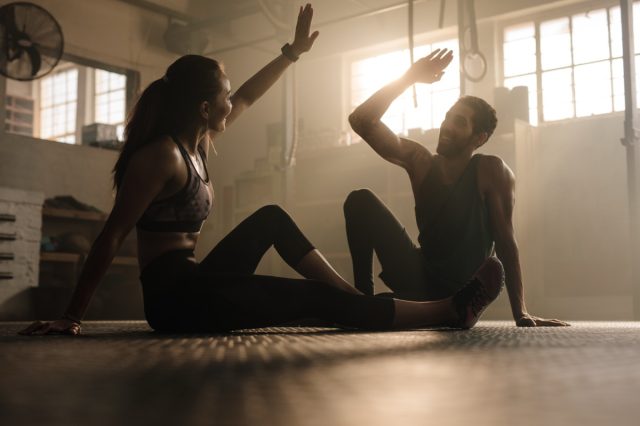 Fitness man and woman giving each other a high five after the training session in gym. Fit couple high five after workout in health club.