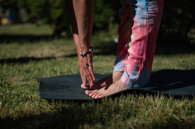 Close-up of a person practicing yoga outdoors on a mat, bending forward with hands touching toes. Relaxing, fitness, and mindfulness in nature.