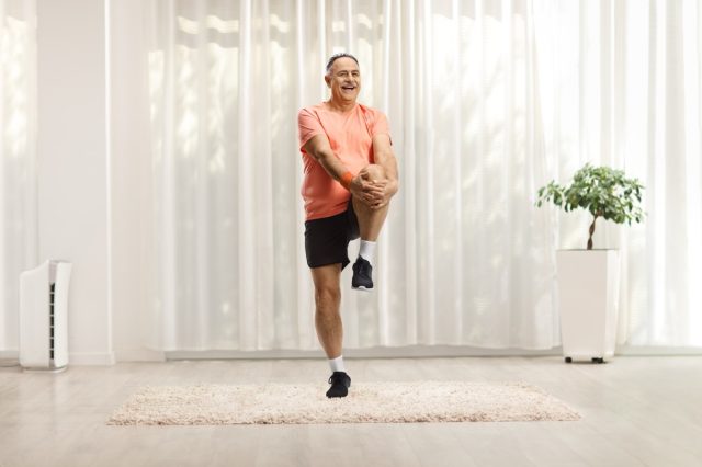 Mature man in sportswear stretching his leg and smiling at home