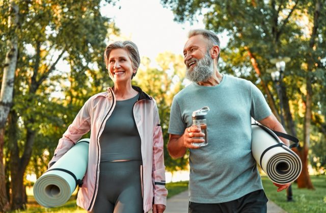 Active life of mature people. Happy sports couple going for a workout outdoors, holding exercise mats and water. Health and recovery, healthy living, hobbies in retirement.
