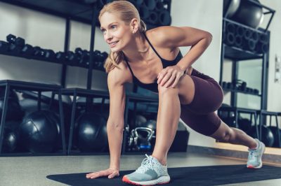 Blonde young woman doing lunges on the mat in the gym