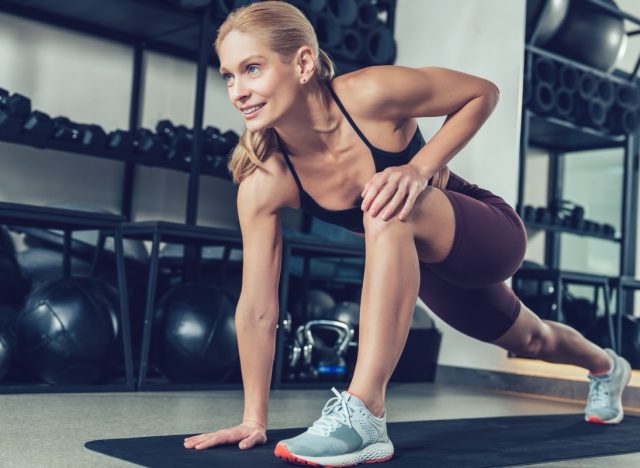 Blonde young woman doing lunges on the mat in the gym