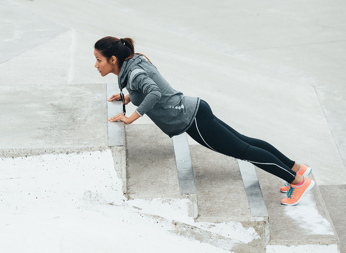 Urban fitness woman workout doing feet elevated push ups and exercising outdoor. Motivated female athlete training hard.