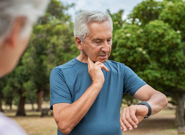 Senior tired man checking pulse after workout. Old man measuring heart rate pulse on his neck and looking sport watch. Aged man times the pulsations at park.