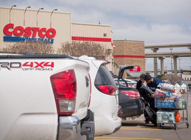 An American family load groceries into car trunk from full shopping carts of essential needs. View from parking load outside of Costco Wholesale store in Lewisville, Texas