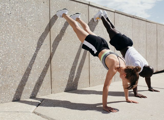 Black man and a white woman perform the vertical plank exercise with their hands on the ground and their feet resting on the wall