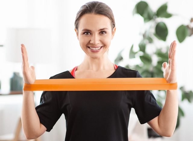 Smile woman exercising with latex resistance band in living room. Workout at home with fitnessband