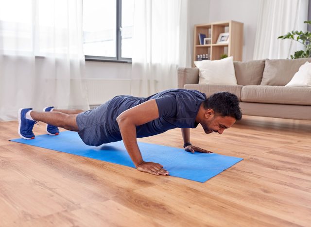 fitness, sport, training and concept - indian man doing push ups at home