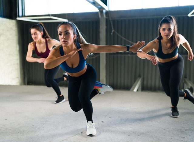 Group of three women doing lateral bounds together in a high-intensity interval class at the gym. Beautiful women in sportswear exercising with a cardio workout