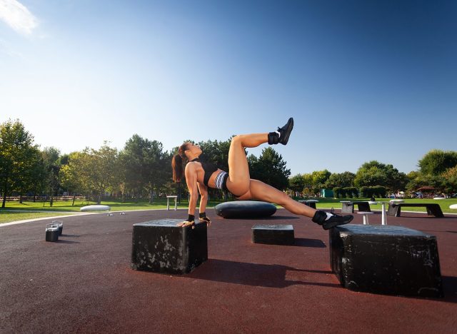 Young fitness woman doing single leg hip thrust in the park.