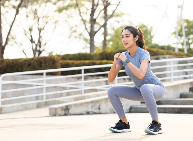 Beautiful fitness asian woman doing squat sit up exercise workout at sport stadium. Attractive female warming up body training wearing sportswear. Healthy and active lifestyle concept.
