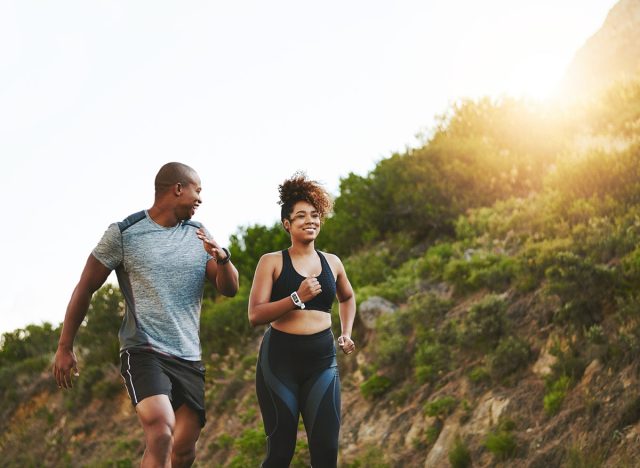 Fitness, nature and couple walking by a mountain training for a race, marathon or competition. Sports, exercise and African athletes or runners doing outdoor running cardio workout together at sunset