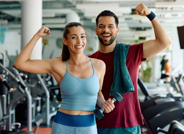 Happy athletic couple flexing their muscles after working out in a gym and looking at camera.