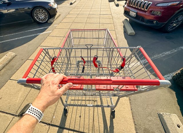 Wide view of a man's hand pushing a large shopping cart, top-down view.