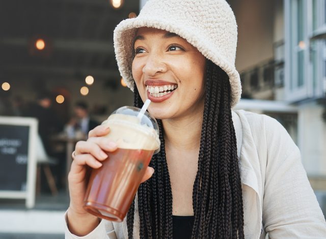 Happy woman, smoothie and smile outdoor at a restaurant and drink from cafe. Milkshake, coffee shop and gen z fashion of a female person relax with drinking from a straw on break on diner patio