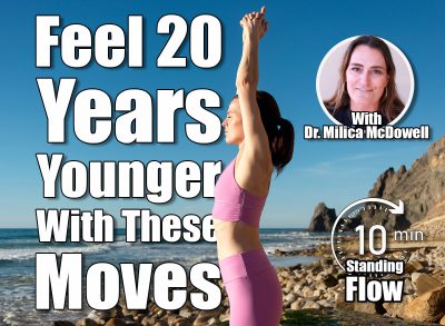 woman standing on rocks by the sea meditating and practicing yoga, arms above head, 5 Simple Standing Exercises That Make You Feel 20 Years Younger, Cover