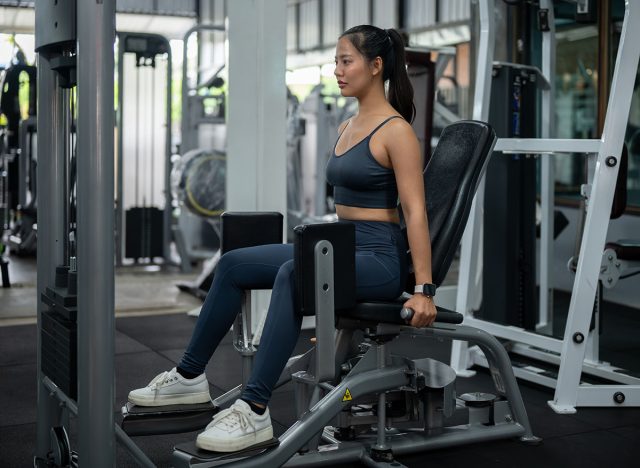 A sporty, strong Asian woman in sportswear is exercising on a hip abduction, adduction machine in the gym, focusing on training her glute muscles. people and sport concepts