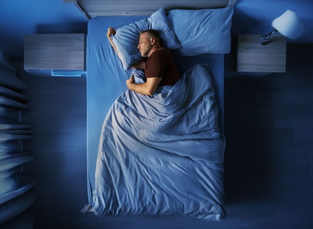 Top view of single middle aged man peacefully sleeping alone in bed at night at home, full length horizontal shot with free space
