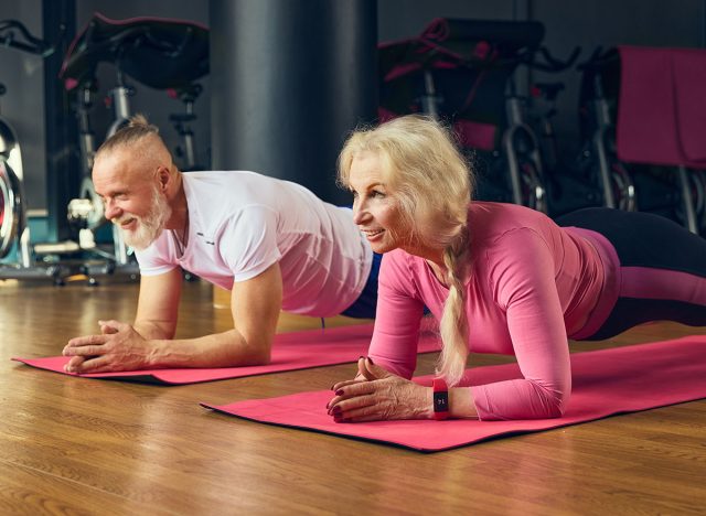 Senior man and woman training, standing in plank position on yoga mats in fitness studio, focusing on core strength and stability. Concept of elderly people, sport, active lifestyle, health