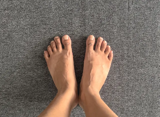 Bare human feet are displayed on a textured gray carpet, providing a neutral yet textured background. This minimalistic scene captures the natural state and positioning of feet in a simple, casual man