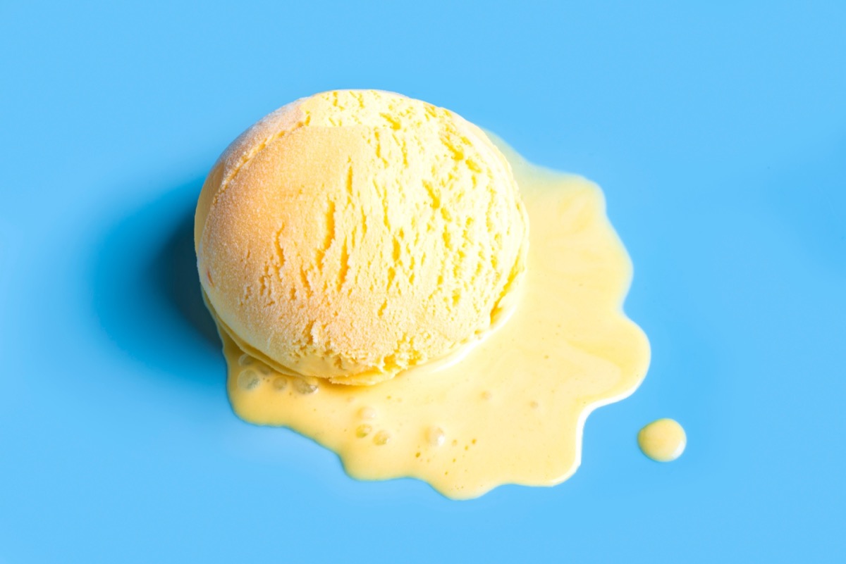 Summer creative concept with melting yellow ice cream scoop on blue background, copy space. Trendy beach relax and summer vacation theme.