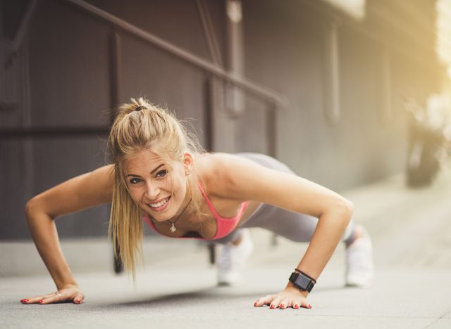 Raising her fitness game. Young smiling women exercise pushups at the street.