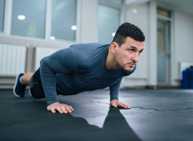 Handsome athlete doing push-ups indoors. Low angle image.
