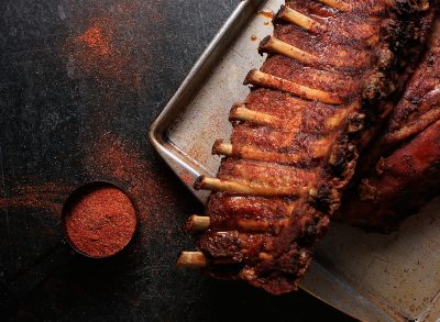 Dark and moody rack of meaty baby back ribs with spicy dry rib rub seasoning on a worn metal sheet pan