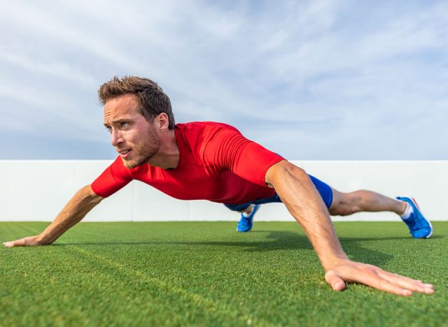 Wide grip pushup push-up variation advanced chest exercise demonstration by male trainer athlete man training at outdoor gym.