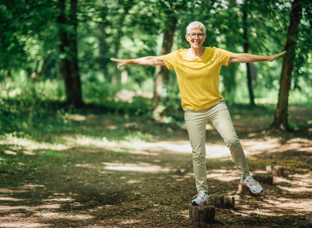 Balancing exercise outdoors. Mature woman standing on one leg, exercising balance
