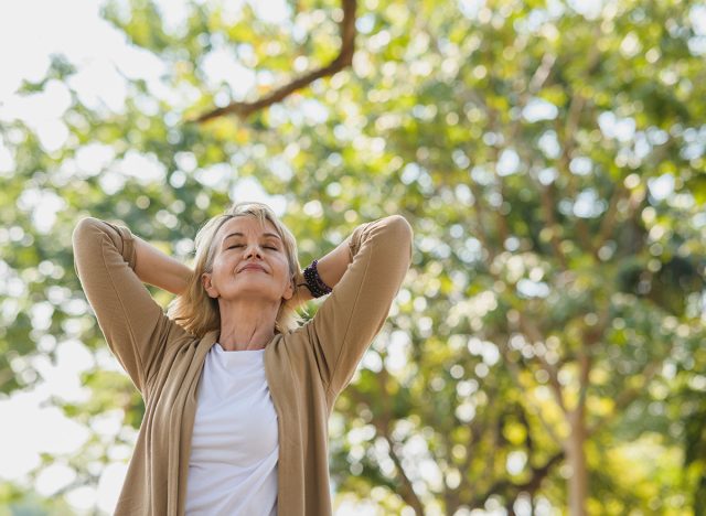 Portrait photo of happy senior Caucasian woman relaxing and breathing fresh air with sunlight in outdoors park. Elderly woman enjoying a day in the park on summer. Healthcare lifestyle and wellness