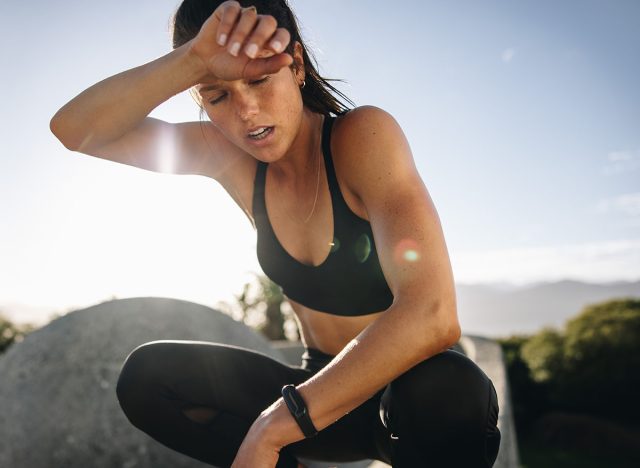 Tired woman sitting and resting after workout. Woman feeling exhausted after training session wiping her sweat from her forehead.
