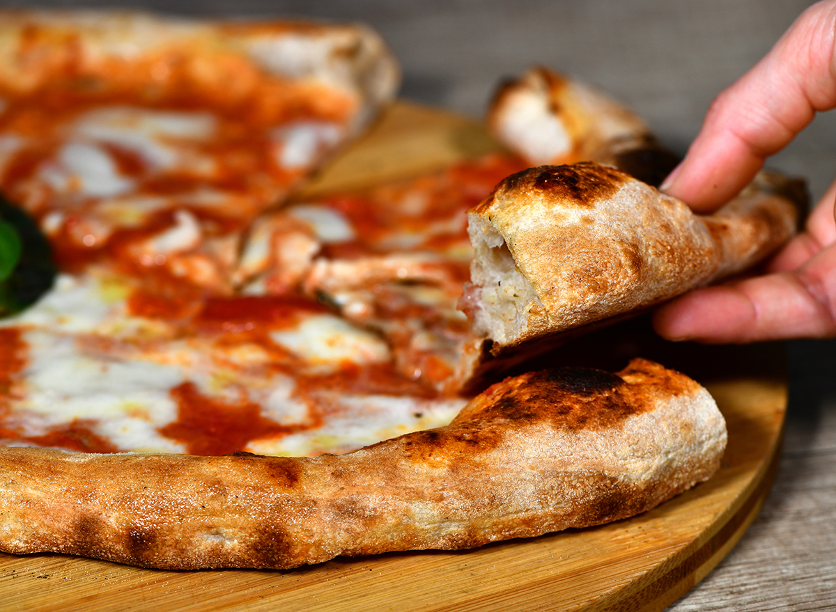 A girl's hand takes a slice of high-dough Neapolitan margherita pizza based on mozzarella, cheese, buffalo mozzarella, tomato sauce, basil
