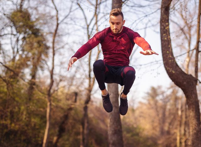 Athletic young man exercising outdoors in a street workout park on a sunny autumn day, jumping over the bench