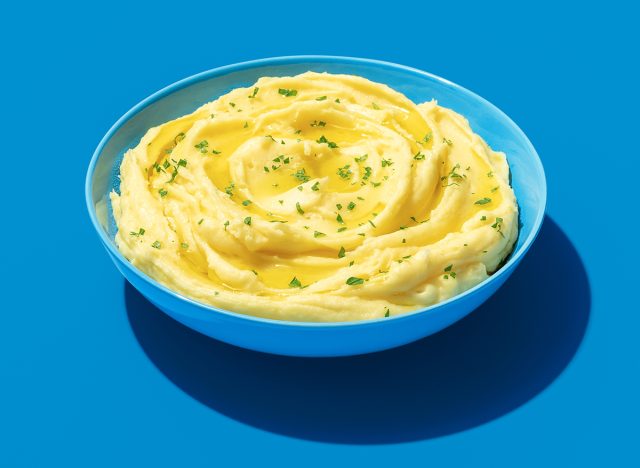 Creamy mashed potatoes topped with green parsley in bright light on a blue table. Bowl with mashed potatoes minimalist on a colorful background