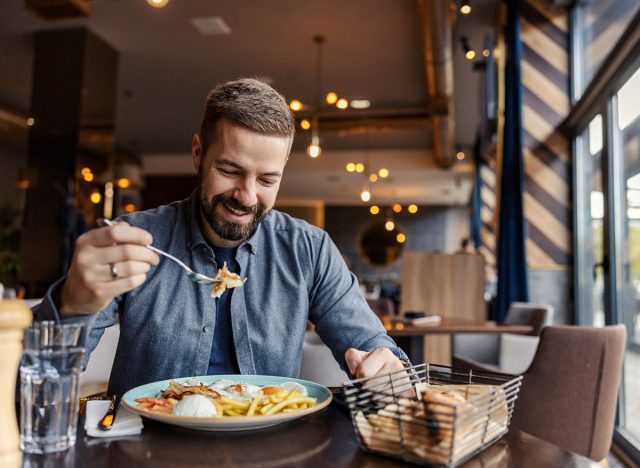 A cheerful man is eating eggs for breakfast at the restaurant.