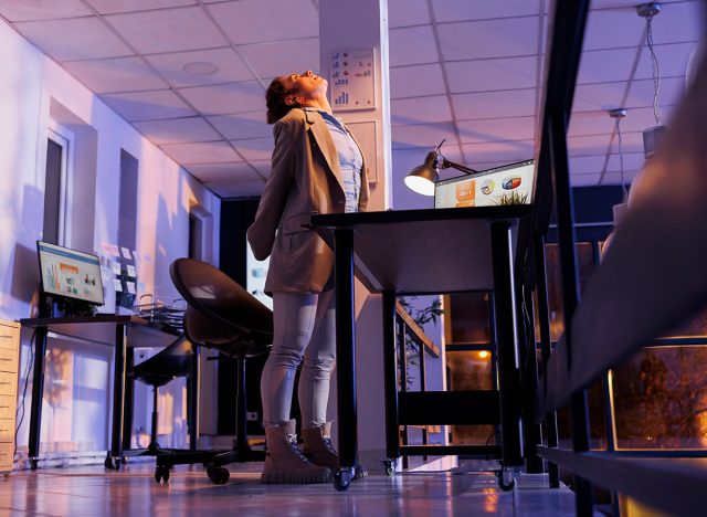 Tired entrepreneur standing up and streching neck after working overhours at company strategy, analyzing financial graph report in startup office. Corporate worker planning investment plan