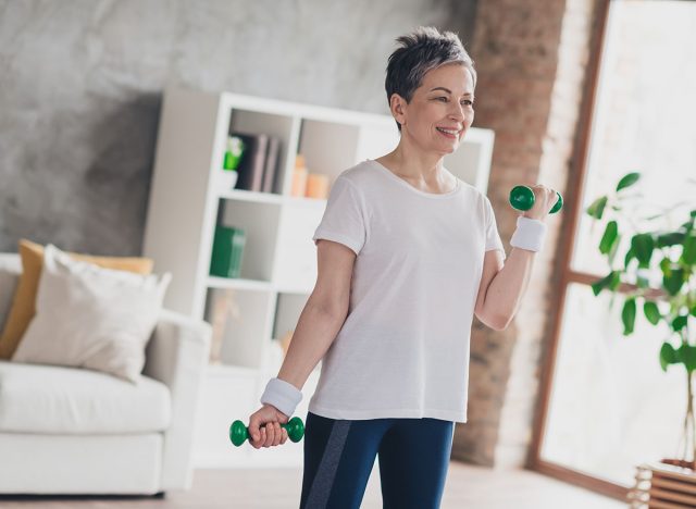 Photo of nice retired woman dumbbells exercises sportswear sport healthy lifestyle workout modern apartment home living room