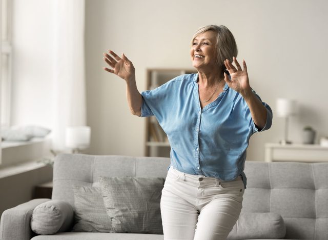 Smiling mature woman moves to favourite song in living room, enjoy active leisure alone at home entertaining, having fun, dancing energetically, exude happiness and carelessness, relish retired life