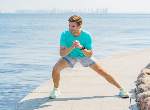 Man exercises by the waterfront in a blue shirt and shorts on a sunny day