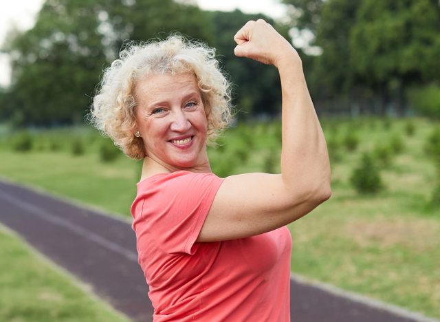 Portrait of a middle aged woman exercising outdoor, workout and training in park. Mature female person happy doing cardio exercise for health, walking or running outside, showing raised arms