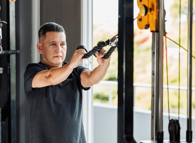Southeast Asian man in his 50s performing face pulls with a rope attachment at an open-air gym to target rear delts.