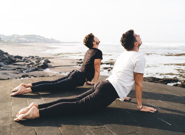 Morning yoga with two focused men in cobra pose symbolizes digital-age alignment—strengthening spine and boosting clarity for navigating high-input environments with centered intention.