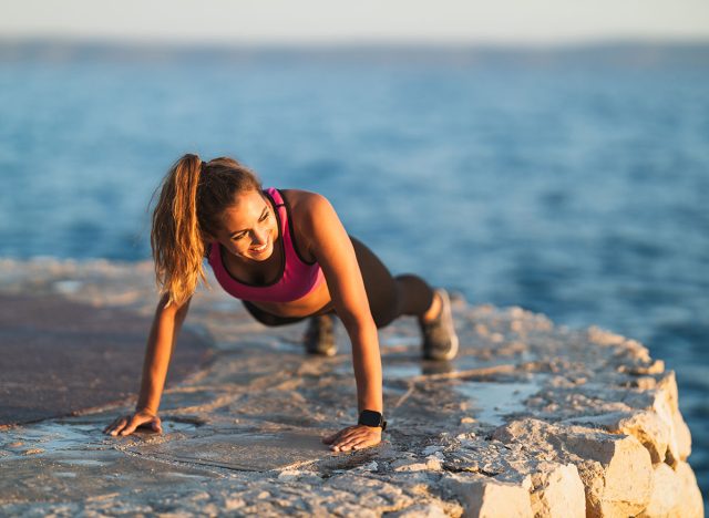Happy young woman doing push-up exercises during hard training near the sea beach